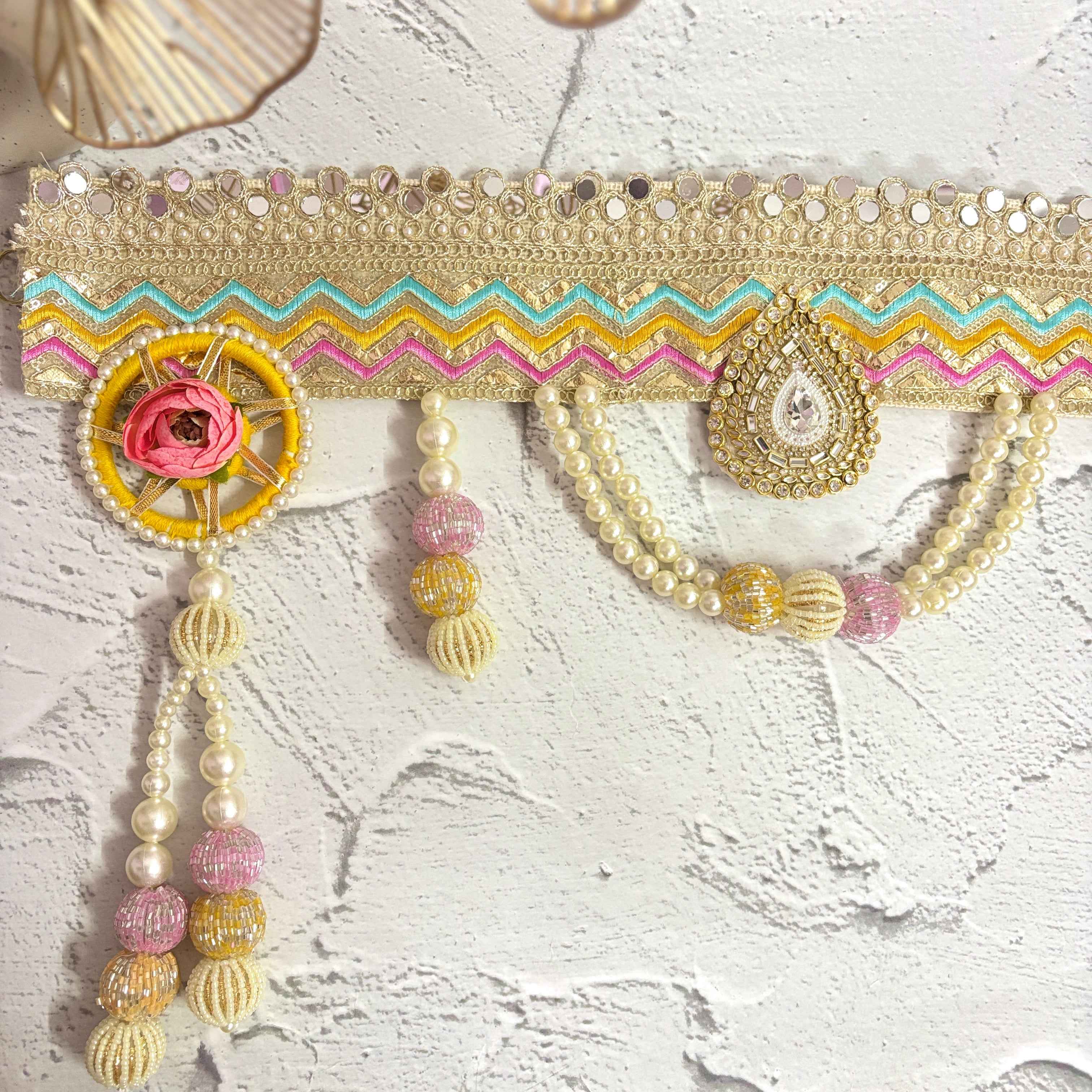 Close-up of the Utsav Leher handmade bandarwal with a gold, pink, yellow, and blue zigzag design. The image highlights the intricate mirror work, pearls, and beaded tassels