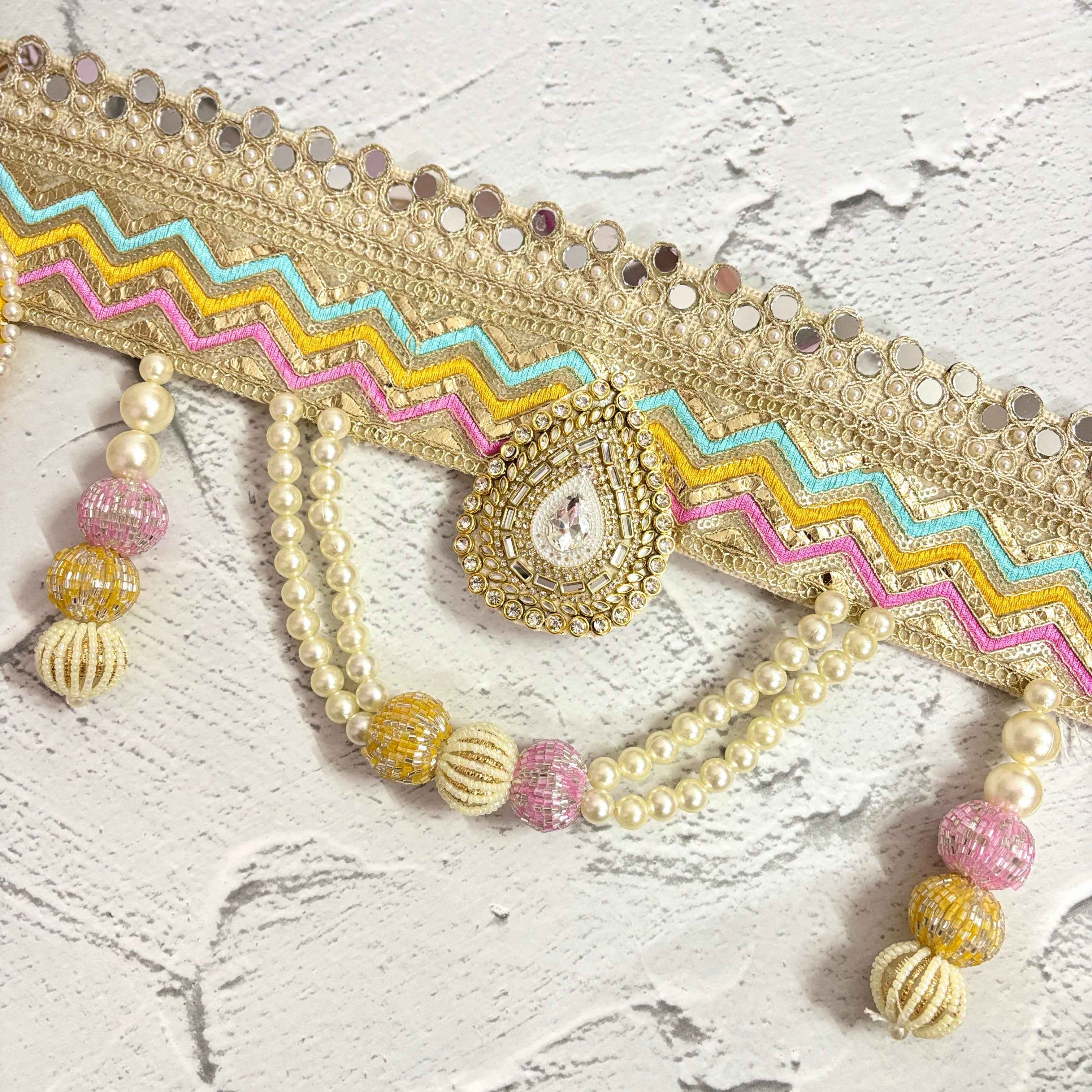 Close-up of the Utsav Leher handmade bandarwal with a gold, pink, yellow, and blue zigzag design. The image highlights the intricate mirror work, pearls, and beaded tassels