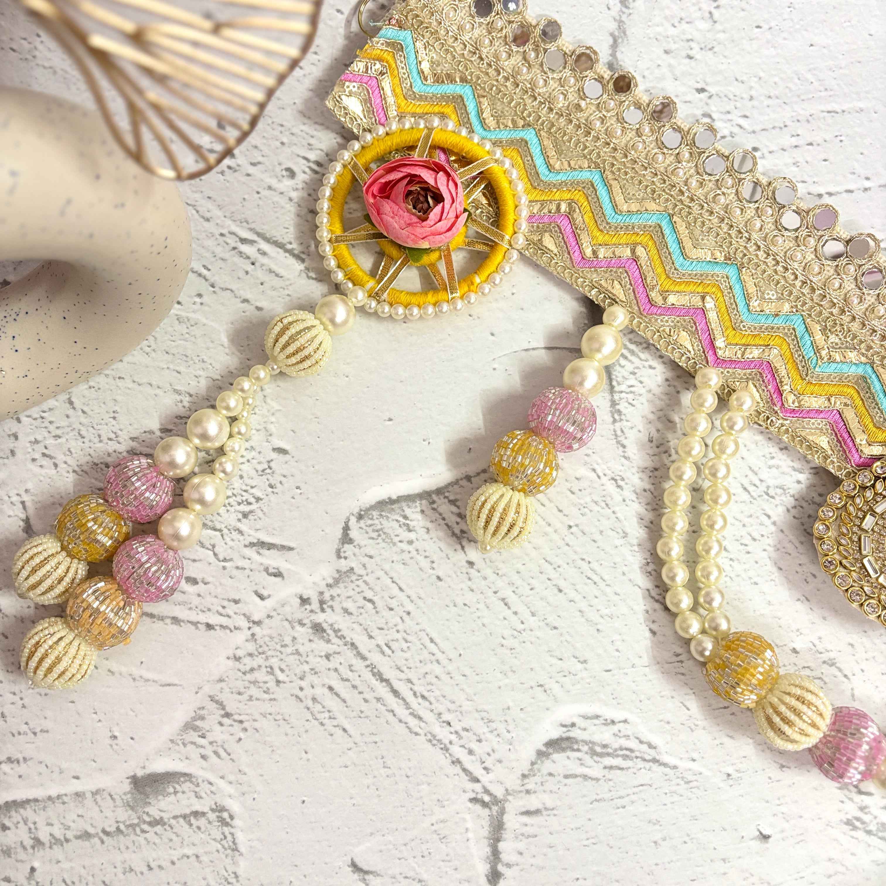 Close-up of the Utsav Leher handmade bandarwal with a gold, pink, yellow, and blue zigzag design. The image highlights the intricate mirror work, pearls, and beaded tassels