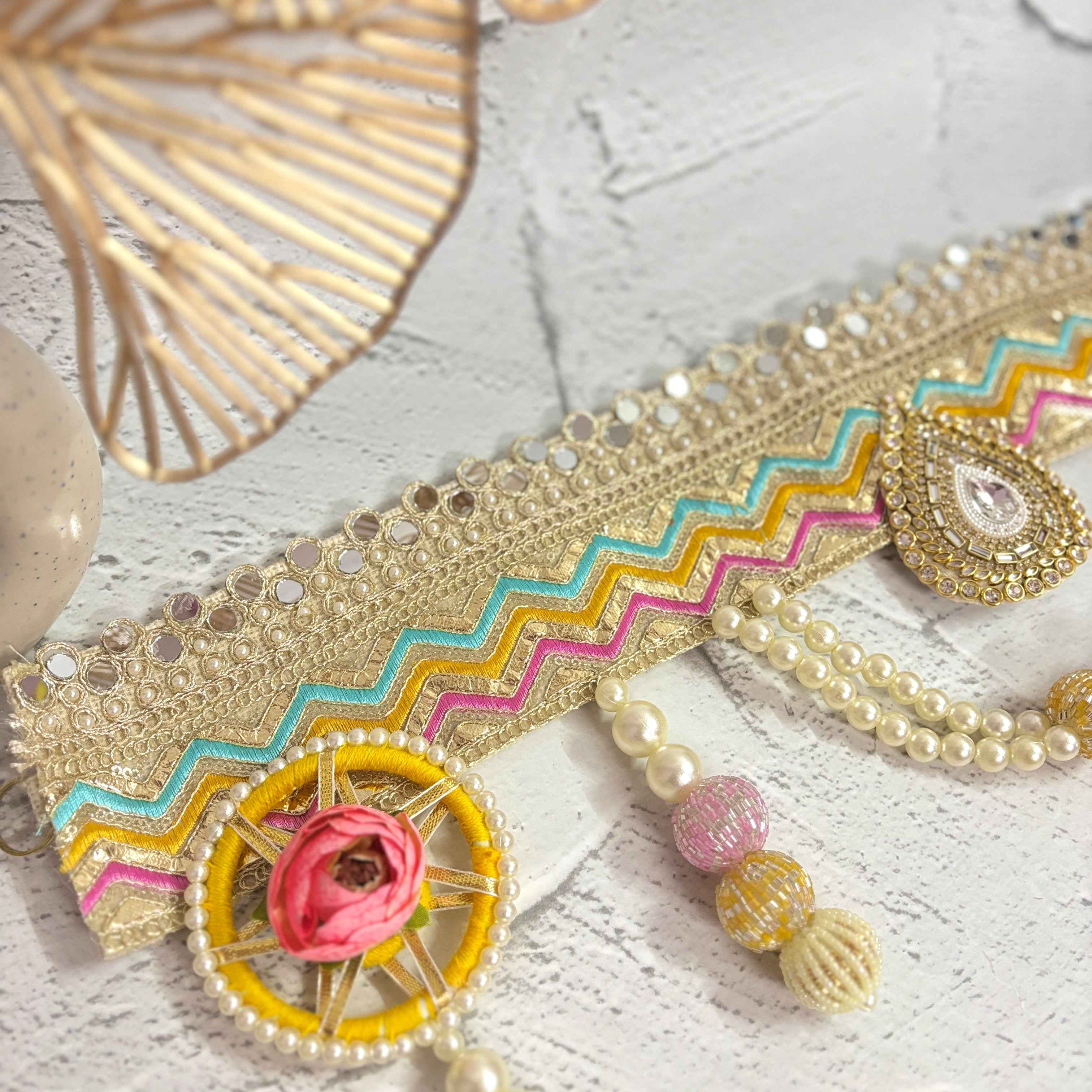 Close-up of the Utsav Leher handmade bandarwal with a gold, pink, yellow, and blue zigzag design. The image highlights the intricate mirror work, pearls, and beaded tassels
